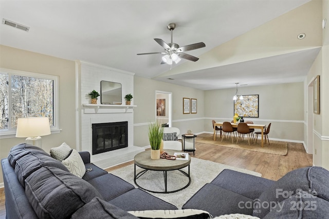 living room featuring visible vents, a brick fireplace, vaulted ceiling, wood finished floors, and baseboards