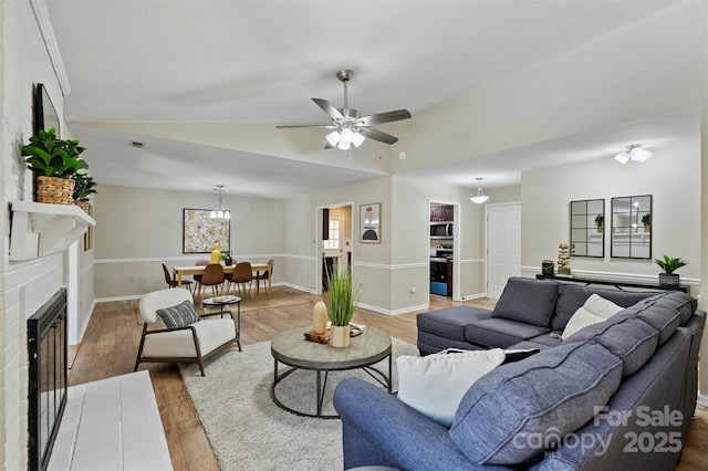 living area featuring a ceiling fan, a brick fireplace, vaulted ceiling, wood finished floors, and baseboards