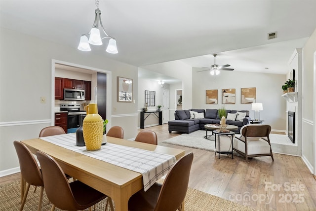 dining space with a glass covered fireplace, visible vents, vaulted ceiling, and light wood finished floors