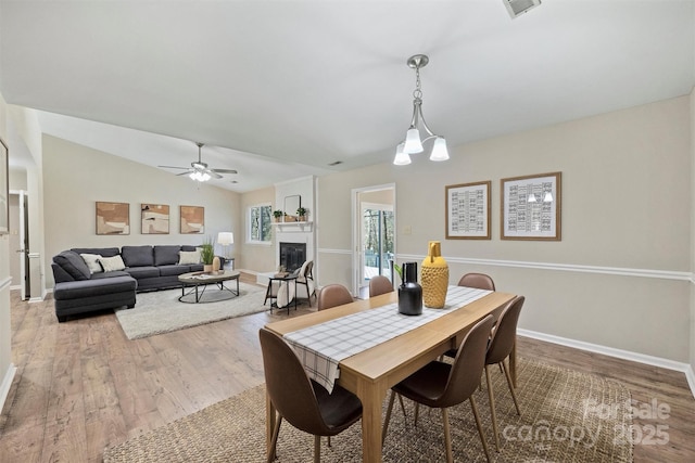 dining space with lofted ceiling, a fireplace, wood finished floors, and visible vents