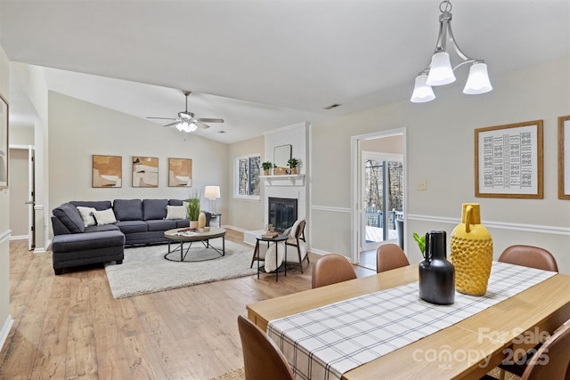 dining area with light wood finished floors, a large fireplace, visible vents, a ceiling fan, and vaulted ceiling