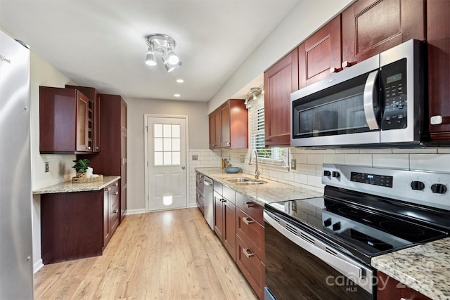 kitchen featuring light stone counters, decorative backsplash, appliances with stainless steel finishes, light wood-style floors, and a sink