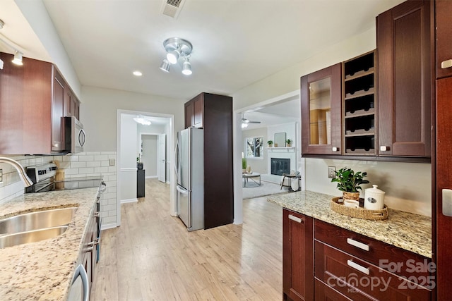 kitchen featuring visible vents, appliances with stainless steel finishes, light wood-type flooring, decorative backsplash, and a glass covered fireplace