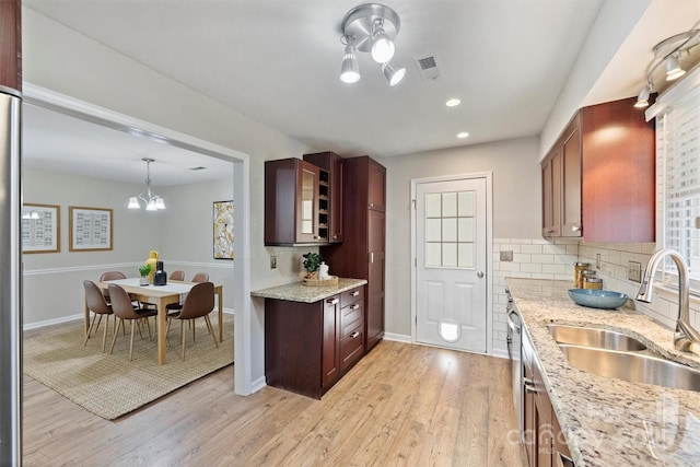 kitchen featuring visible vents, light wood-style flooring, decorative backsplash, a sink, and a chandelier