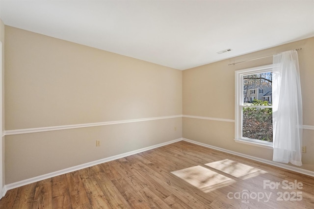 empty room featuring wood finished floors, visible vents, and baseboards