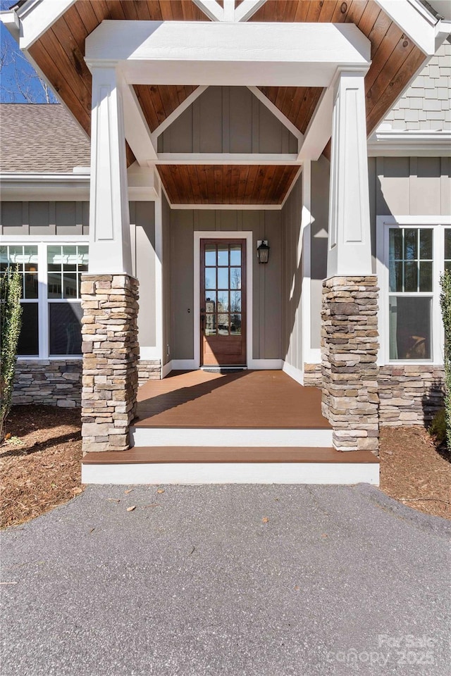 doorway to property with board and batten siding, stone siding, and a porch