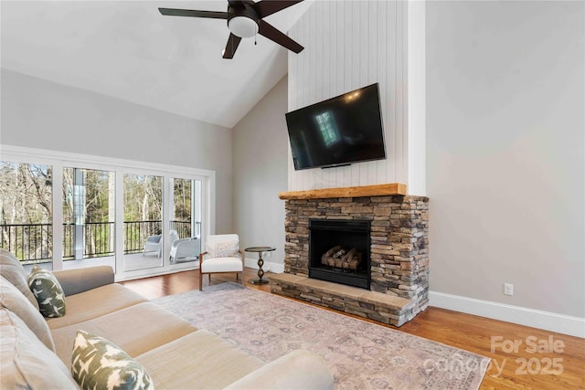 living area featuring high vaulted ceiling, a stone fireplace, wood finished floors, a ceiling fan, and baseboards