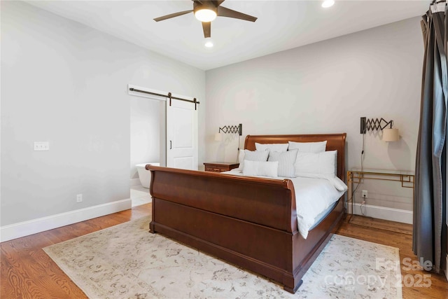 bedroom featuring ceiling fan, a barn door, recessed lighting, wood finished floors, and baseboards