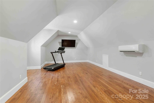 exercise room with lofted ceiling, a wall mounted air conditioner, wood finished floors, and baseboards