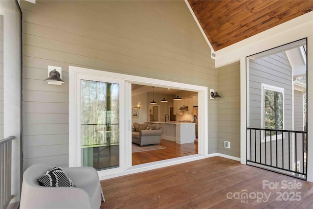 interior space with wood ceiling, a sink, wooden walls, wood finished floors, and high vaulted ceiling