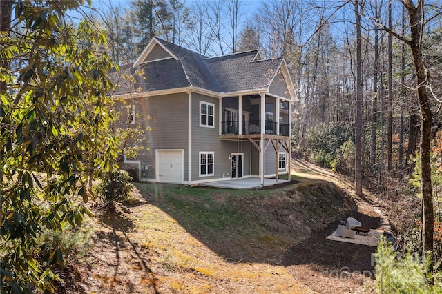 back of property featuring a lawn, a sunroom, roof with shingles, an attached garage, and a patio area