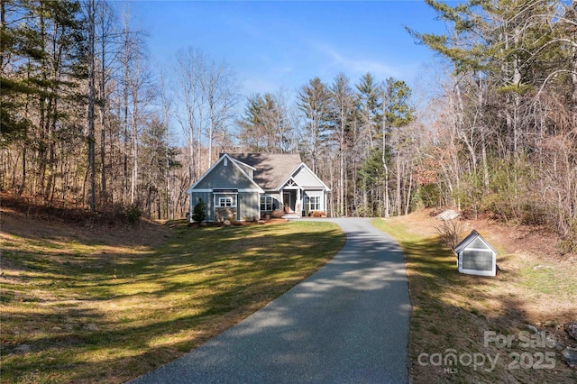 view of front of property featuring aphalt driveway, a front yard, and a view of trees