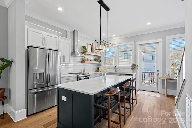 kitchen featuring a center island, ornamental molding, decorative backsplash, appliances with stainless steel finishes, and wall chimney exhaust hood