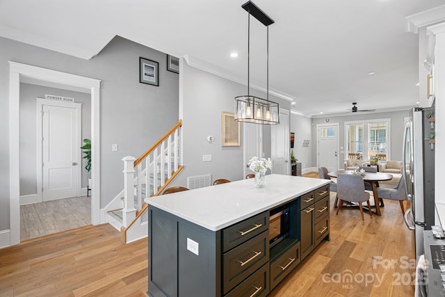 kitchen featuring light wood-style flooring, a center island, appliances with stainless steel finishes, crown molding, and light countertops