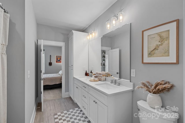 ensuite bathroom with toilet, a sink, connected bathroom, double vanity, and baseboards