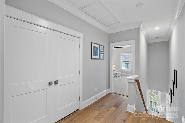 hall with baseboards, attic access, light wood-type flooring, ornamental molding, and an upstairs landing