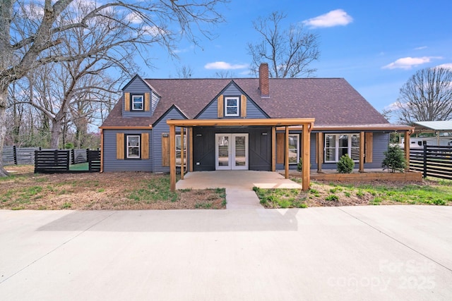 view of front facade with a chimney, fence, french doors, and a shingled roof