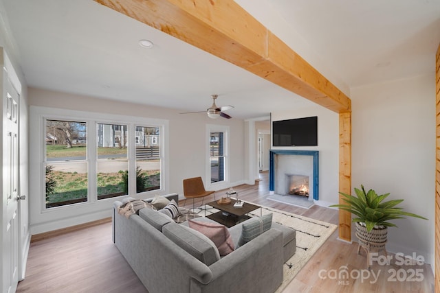 living room featuring a lit fireplace, healthy amount of natural light, wood finished floors, and baseboards