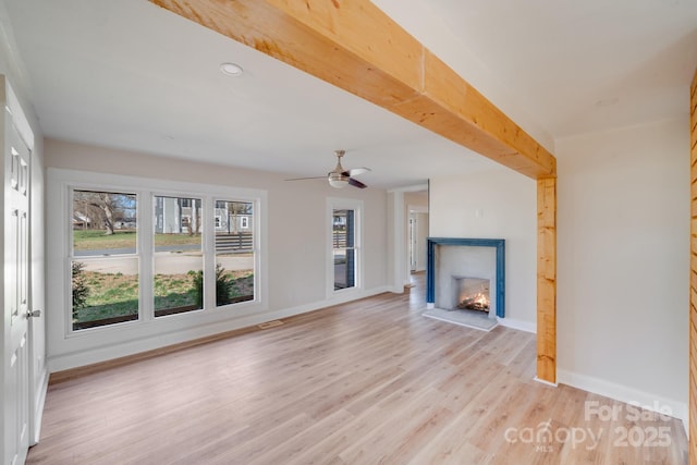 unfurnished living room featuring light wood finished floors, baseboards, a lit fireplace, and a ceiling fan