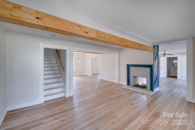 unfurnished living room with light wood-style floors, stairway, baseboards, and a multi sided fireplace