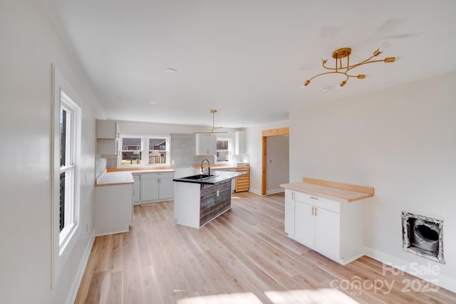 kitchen with light wood-style floors, a sink, a kitchen island, and white cabinetry