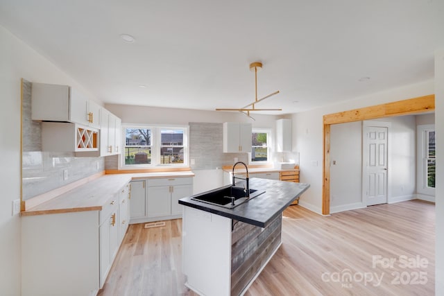 kitchen featuring a sink, light wood-style flooring, backsplash, white cabinetry, and recessed lighting