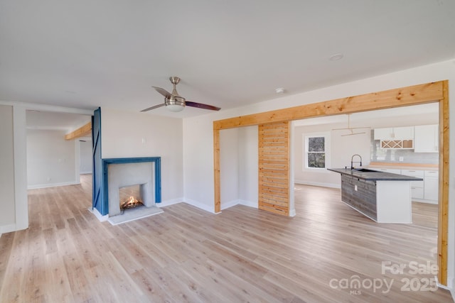 unfurnished living room featuring a sink, light wood finished floors, a multi sided fireplace, ceiling fan, and baseboards