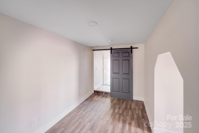 unfurnished room featuring a barn door, wood finished floors, and baseboards