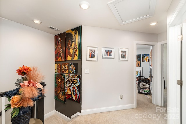 hall with visible vents, baseboards, and light colored carpet