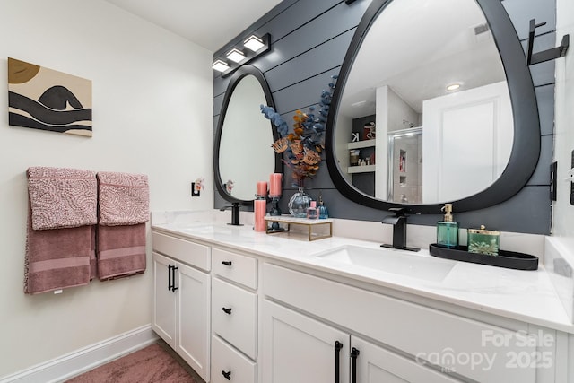 bathroom featuring a stall shower, a sink, baseboards, and double vanity