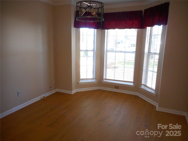 empty room with plenty of natural light, baseboards, an inviting chandelier, and wood finished floors