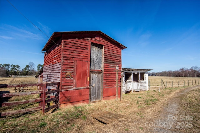 view of outbuilding with a rural view, fence, and an outbuilding