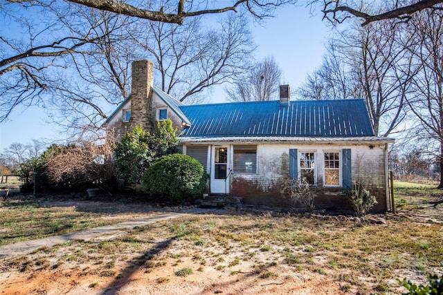 view of front of property with entry steps, a chimney, metal roof, and brick siding