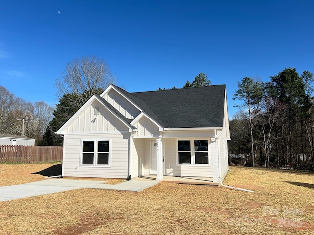 modern inspired farmhouse with roof with shingles, board and batten siding, a front yard, and fence