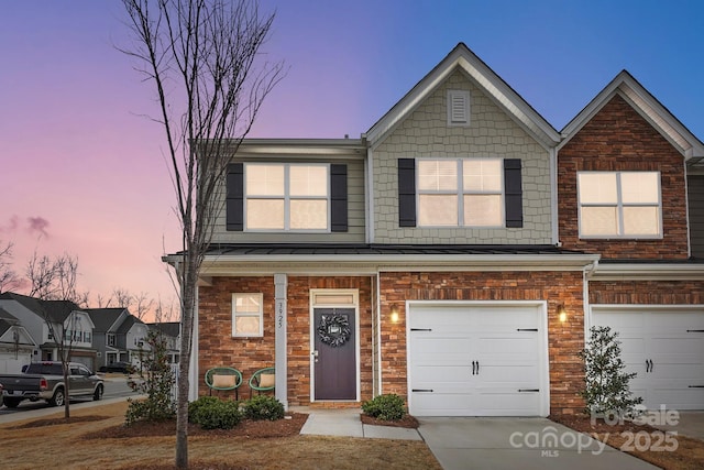 townhome / multi-family property featuring a garage, concrete driveway, metal roof, a standing seam roof, and brick siding