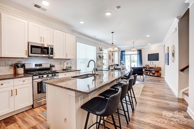 kitchen with appliances with stainless steel finishes, a sink, visible vents, and crown molding