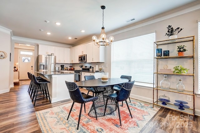 dining space with a chandelier, visible vents, baseboards, light wood finished floors, and crown molding