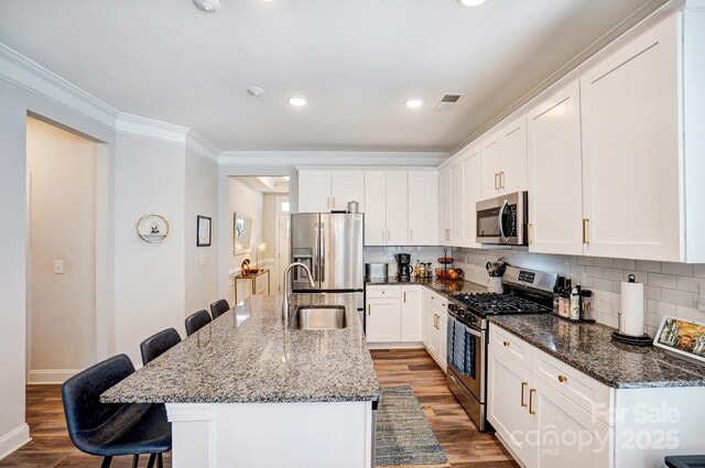 kitchen featuring wood finished floors, visible vents, a kitchen breakfast bar, ornamental molding, and appliances with stainless steel finishes