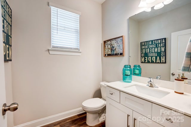 half bathroom featuring toilet, baseboards, wood finished floors, and vanity