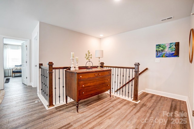 hall with light wood-style flooring, visible vents, baseboards, and an upstairs landing