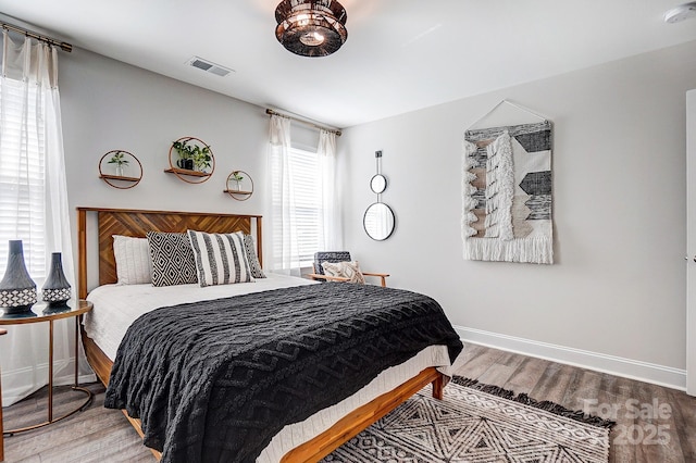 bedroom with baseboards, visible vents, and wood finished floors