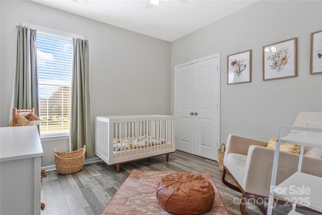 bedroom featuring ceiling fan, a crib, baseboards, and wood finished floors