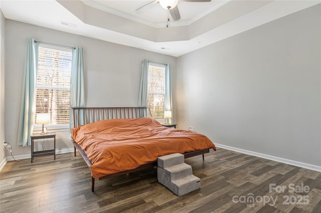 bedroom with wood finished floors, multiple windows, a raised ceiling, and baseboards