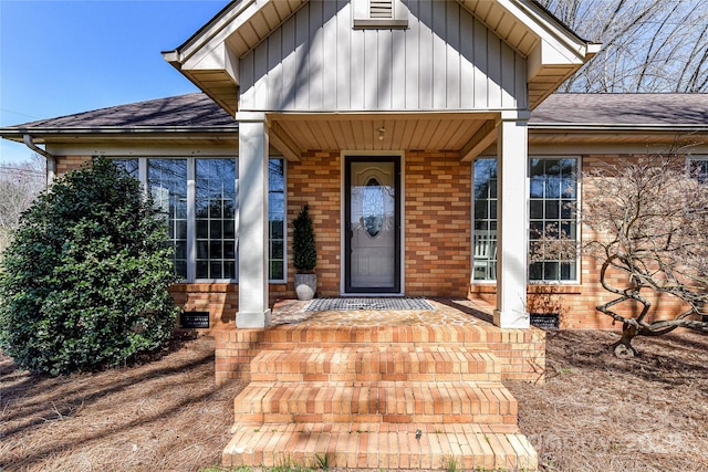 view of exterior entry with covered porch, brick siding, roof with shingles, and crawl space