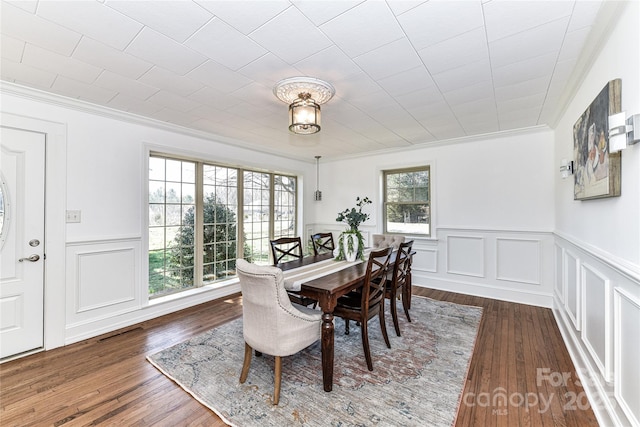 dining area featuring a decorative wall, crown molding, visible vents, and wood finished floors