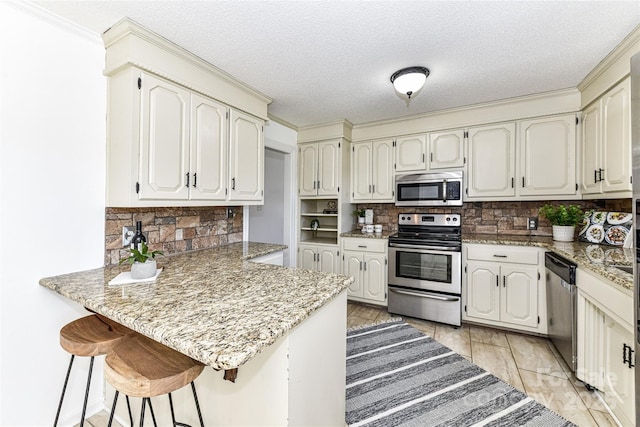 kitchen featuring tasteful backsplash, a textured ceiling, stainless steel appliances, a peninsula, and a breakfast bar area