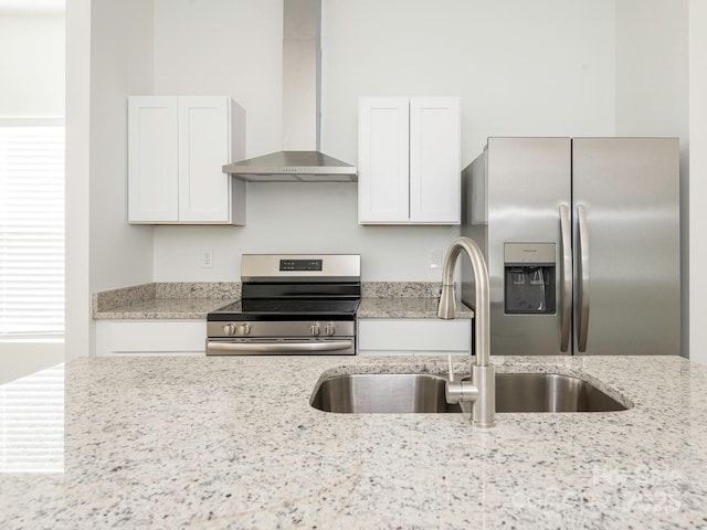 kitchen featuring wall chimney range hood, appliances with stainless steel finishes, white cabinets, and a sink