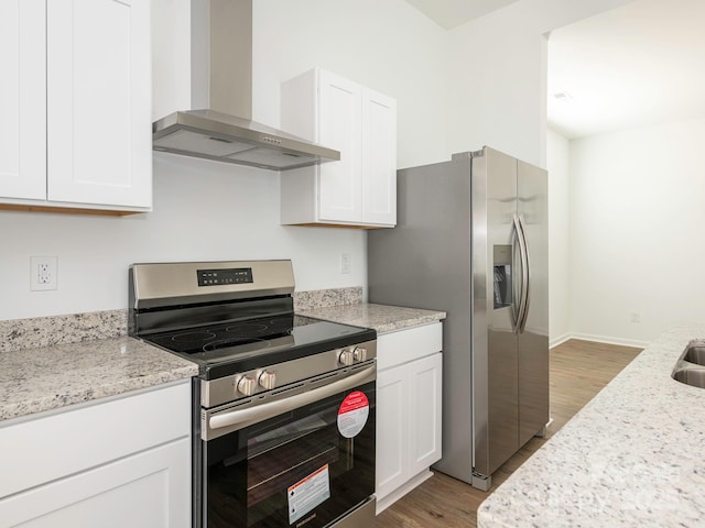 kitchen featuring light stone counters, light wood-style flooring, stainless steel appliances, white cabinets, and wall chimney exhaust hood