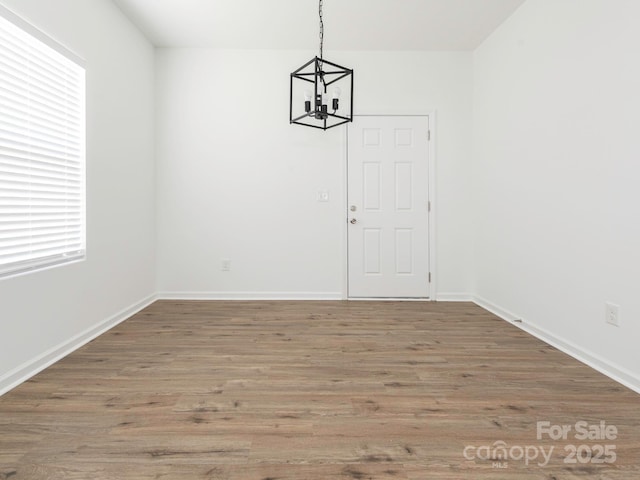 unfurnished dining area with a notable chandelier, baseboards, and wood finished floors