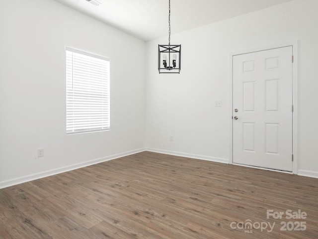 unfurnished dining area featuring baseboards, a chandelier, and wood finished floors